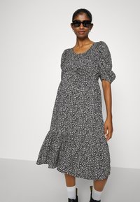 Vestido preto e branco com padrão, decote arredondado, mangas bufantes, saia em camadas, e usado com óculos de sol pretos e meias brancas.