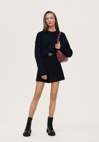 Suéter de canalé azul marino, pantalones cortos negros a medida, botas negras con cordones y un bolso de hombro burdeos. Incluye un cinturón con detalles en dorado.