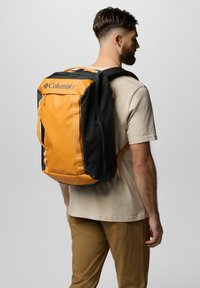 Columbia-Rucksack mit schwarzem Gehäuse und orangefarbenen Akzenten, aus strapazierfähigem Material, rechteckiger Form und sichtbaren Reißverschlüssen und Griffen.