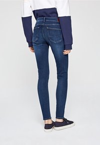 Smal jeans i mörkblå denim med en slät yta, bakfickor och hög midja, i kombination med mörka snörskor.