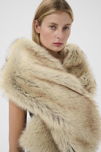Tânără cu părul blond purtând un șal din blană artificială cu dungi bej și maro, pe un fundal alb simplu.