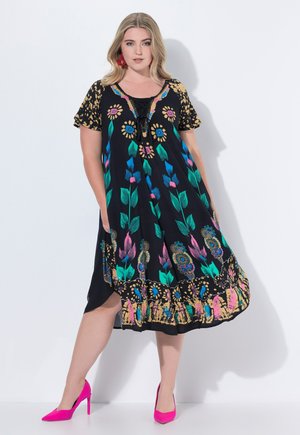 Schwarzes Kleid mit floralem Stickmuster in Blau, Rosa und Grün. Verfügt über einen V-Ausschnitt mit Schnürdetails und einem gerafften Saum. Getragen mit rosa Absätzen.