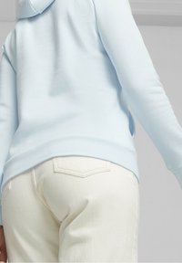 Felpa con cappuccio azzurro chiaro a maniche lunghe con trama a coste e cappuccio, abbinata a jeans di denim color crema con due tasche posteriori.