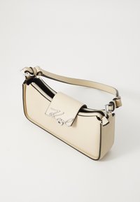 Cream-colored handbag with black accents, featuring a zip closure, a metal logo detail, and an adjustable strap. Smooth texture and rectangular shape.