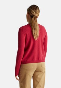 Červený pletený svetr s kulatým výstřihem, dlouhými rukávy a měkkou texturou. Spodní okraj a manžety jsou žebrované pro přiléhavý vzhled.