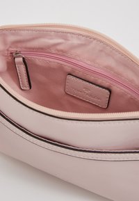 Vaaleanpunainen keinokuitukäsilaukku, jossa on vetoketjupussi ja logotagi. Sujuva rakenne, pyöreä muoto ja erottuvat pistot.