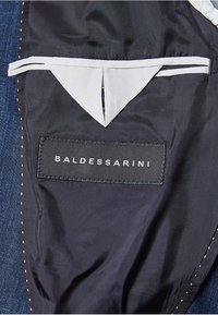 Czarna podszewka materiałowa wewnątrz kurtki z białym trójkątnym detalem kieszeni oraz naszywką z haftowanym logo marki Baldessarini.