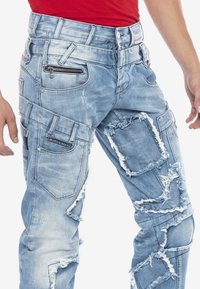 Helle blaue Jeans aus Denim mit abgetragenen Flecken und fransigen Kanten. Verfügt über mehrere Taschen, ein Reißverschlussdetail und ein lockeres Schnittdesign.