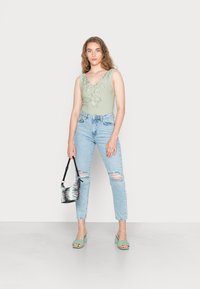 Top sem mangas verde-claro com decote bordado, jeans azul-claro desfiados, sandálias de salto verde-menta e bolsa preta e branca com padrão.