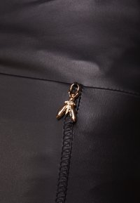 Black fabric with a smooth texture features a gold zipper pull shaped like a insect, accentuating the design detail along the seam.