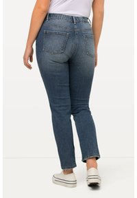 Džínové kalhoty v středně modré barvě s úzkým pasem a rovnýma nohama. Mají dvě zadní kapsy a hladký, mírně texturovaný povrch.