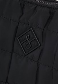 Chaqueta acolchada negra con un patrón de acolchado, textura suave y un pequeño logo en relieve en forma de cuadrado en la tela.