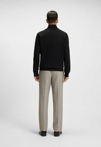 Felpa nera con zip e colletto alto, abbinata a pantaloni a quadri grigi chiari e scarpe nere, vista di spalle.