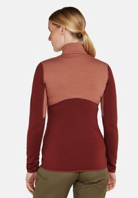 Camiseta de manga larga con cuello alto, diseño a bloques de color en óxido y marrón claro, tela texturizada y silueta ajustada.