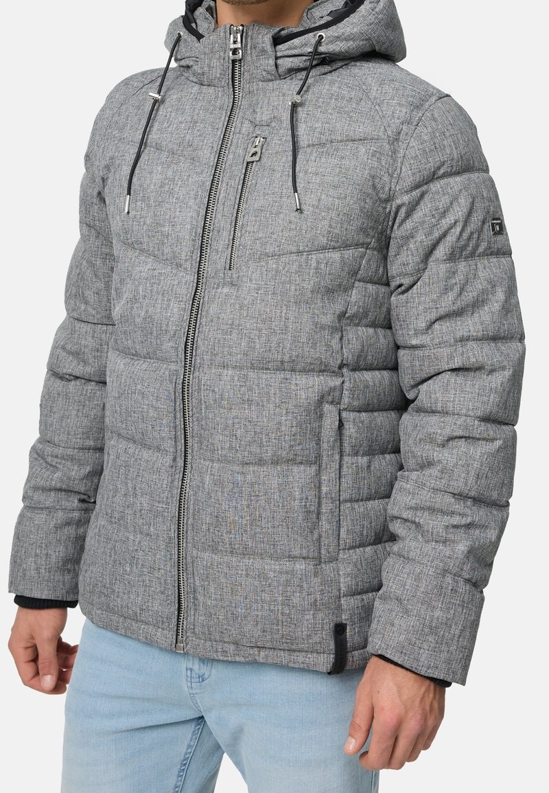 Graue Steppjacke mit Kapuze, vorne mit Reißverschluss, gesteppten Nähten und verstellbaren Kordelzügen. Das Material hat eine strukturierte Oberfläche.