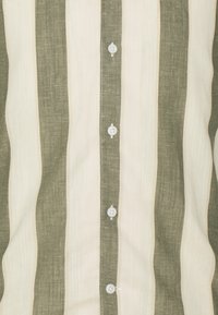 Camisa de botones a rayas con amplias rayas en color blanco roto y verde olivo, confeccionada en una tela ligera y con botones blancos en el frente.