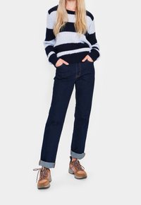 Blue and navy striped knit sweater, dark denim jeans, and brown hiking boots with laces; cuffs of jeans are rolled up.