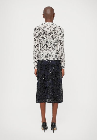 Floral-patterned, long-sleeve top with gathered texture, paired with a knee-length dark navy sequin skirt. Black heels complete the look.