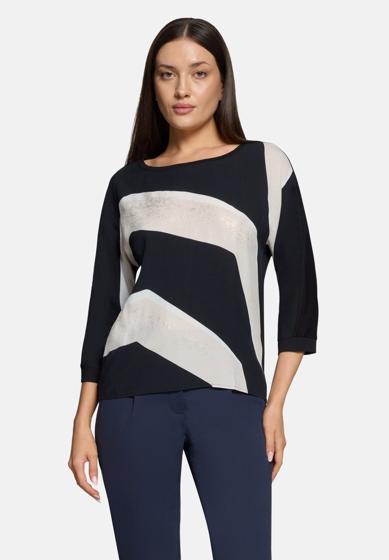 Zwart-crème top met een abstract zigzagpatroon, driekwart mouwen en een ronde halslijn, gemaakt van een glad, lichtgewicht materiaal.