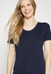 Camiseta de manga curta azul-marinho com decote redondo, feita de um tecido suave e elástico. Apresenta um design ajustado e uma textura macia.