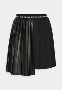 Svart plisserad kjol i konstläder med elastisk midja och vit "Versace Jeans Couture" branding.