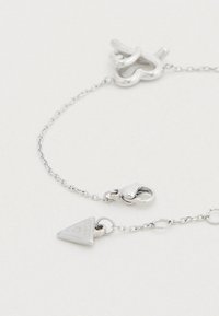 Βραχιόλι αλυσίδας από ασήμι με κούμπωμα σε σχήμα καρδιάς και τρίγωνο με ανάγλυφο κείμενο. Λεπτή υφή και γυαλιστερό φινίρισμα.