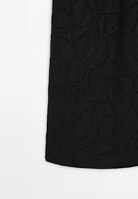 Tissu noir avec un motif irrégulier, surélevé et cousu ressemblant à des formes abstraites de galets sur un fond lisse.