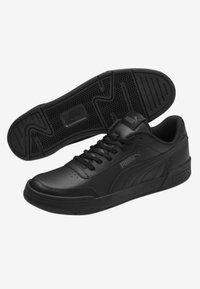 Chaussures de sport noires avec une tige en cuir lisse, un design à lacets, un col rembourré et une semelle extérieure en caoutchouc texturée avec un motif en zigzag.