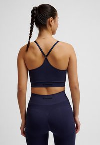 Marineblauw atletisch crop top met kruisbanden en logo-opdruk. De gladde textuur en fitted ontwerp passen perfect bij bijpassende leggings.