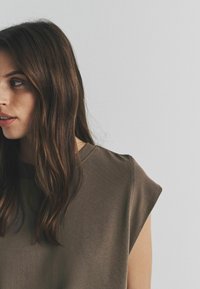 Ruskea, pyöreäkauluksinen paita, jossa on lyhyet hihat ja rento istuvuus. Sileä rakenne ja yksinkertainen muotoilu, jossa on vähäisiä yksityiskohtia.