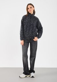 Pulover din fleece cu închidere cu jumătate de fermoar, cu un imprimeu animal în tonuri de gri închis. Asortat cu blugi negri și adidași gri.