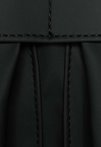 Tissu noir plissé avec des détails de coutures visibles. Texture lisse et couleur homogène avec des lignes et des plis nets pour un design structuré.