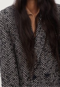 Dwurzędowa marynarka z czarno-białym wzorem w rybią łuskę, teksturowanym materiałem i czarnymi guzikami.