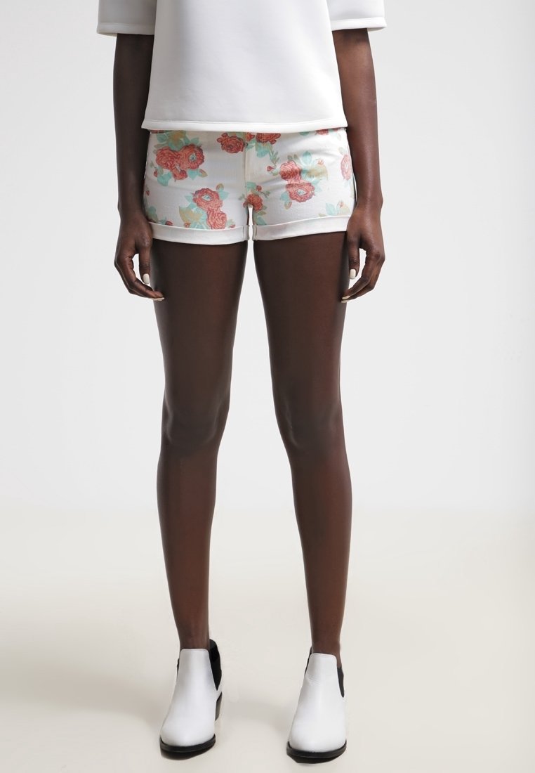 Květinové šortky z bílé látky s motivem červených a tyrkysových růží. Dokončeno bílým přiléhavým topem a černobílými kotníkovými botami.