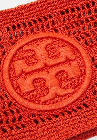 Czerwony pleciony materiał szydełkowy z okrągłym emblematem, z uniesionym wzorem krzyżującym się w centrum.