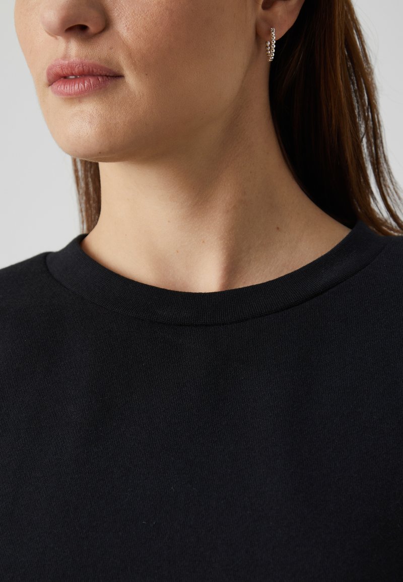 Felpa nera con scollatura rotonda, realizzata in tessuto morbido. Visione ravvicinata che evidenzia la texture liscia e i dettagli minimi.