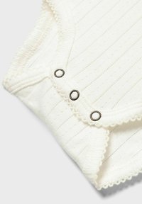 Bodysuit pour bébé blanc avec texture côtelée, doté de trois boutons-pression métalliques et d'une bordure festonnée au niveau de l'encolure et des emmanchures.