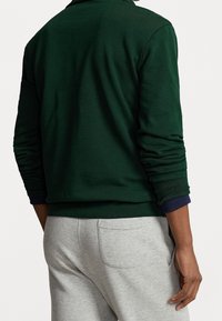Felpa verde con tessuto texture e polsini a coste, abbinata a pantaloni della tuta grigio chiaro con tasca posteriore.