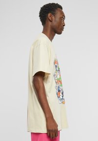 T-shirt en coton beige présentant un imprimé graphique coloré sur le devant, avec des manches courtes et une coupe décontractée, montrant un profil latéral.