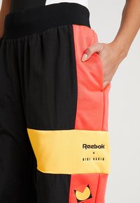 Svarta, korallfärgade och gula sweatpants med avslappnad passform. Har en bred midja och sidofickor, märkta med "Reebok x Gigi Hadid."