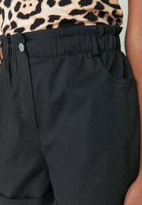 Czarne szorty wykonane z lekkiego materiału, z elastycznym paskiem w talii, bocznymi kieszeniami oraz gładką fakturą. Zbliżenie na materiał.