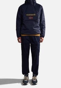 Mörkblå tröja med dragkedja och en logotyp samt en norsk flagga på framsidan, kombinerad med mörkblå cargobyxor och grå sneakers.