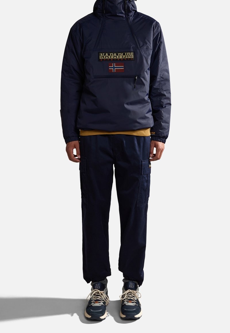Mörkblå tröja med dragkedja och en logotyp samt en norsk flagga på framsidan, kombinerad med mörkblå cargobyxor och grå sneakers.