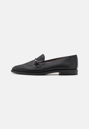 Mocasines de cuero negro con un acabado texturizado, un tacón plano y un acento decorativo de hebilla plateada en el empeine. Diseño suave y minimalista.