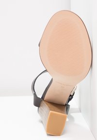 Sandale en cuir noir avec un talon en bois, semelle en caoutchouc beige, taille 37, et "Fabriqué en Espagne" embossé sur la semelle.