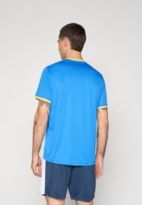Blue athletic t-shirt with short sleeves, round neck, and yellow trim details. Lightweight fabric, smooth texture, worn with navy shorts.