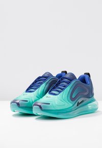 Paire de baskets de sport bleu et turquoise avec semelles amorties visibles, motifs en forme de vagues et fermeture à lacets, placées côte à côte.