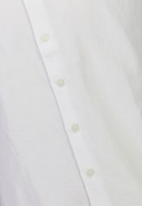 Close-up van witte stof met vier op elkaar genaaide witte knopen, verticaal uitgelijnd op de voorflap van een shirt.