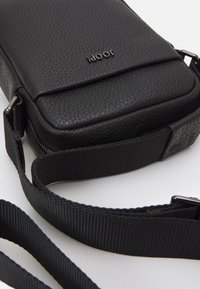 Borsa a tracolla rettangolare nera realizzata in pelle testurizzata, con chiusura a zip e una tracolla in nylon liscia e regolabile.
