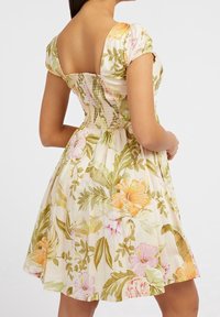 Vestido floral en beige claro con patrones en naranja, rosa y verde. Presenta una espalda cuadrada, mangas cortas abullonadas y un corsé ajustado.